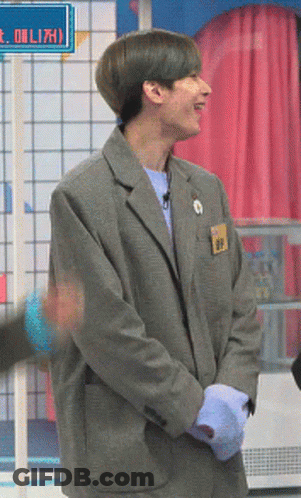 A Man In A Grey Suit Stands In Front Of A Sign That Says ' Eolizh ' On It GIF
