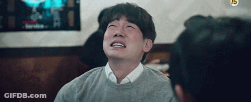A Man In A Grey Sweater Is Crying While Sitting At A Table . GIF