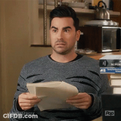 A Man In A Grey Sweater Is Holding A Piece Of Paper In Front Of A Pop Box GIF
