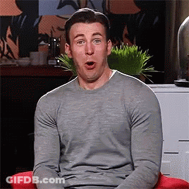 A Man In A Grey Sweater Is Sitting In A Red Chair With His Mouth Open . GIF
