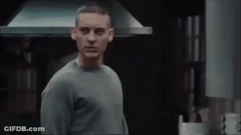 A Man In A Grey Sweater Is Standing In Front Of A Kitchen Hood GIF
