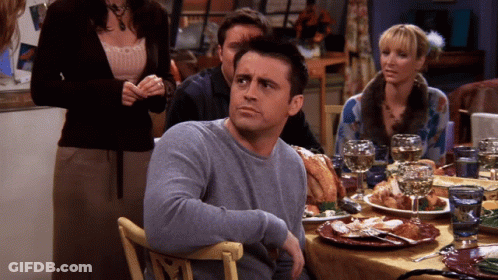 A Man In A Grey Sweater Sits At A Table With Plates Of Food GIF