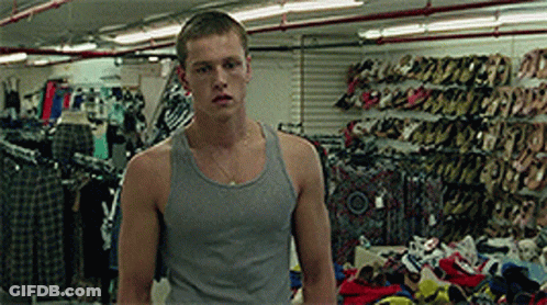 A Man In A Grey Tank Top Is Standing In A Store Full Of Shoes GIF