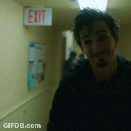 A Man In A Hallway With An Exit Sign Above Him GIF
