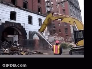 A Man In A Hard Hat Stands In Front Of A Building Being Demolished GIF