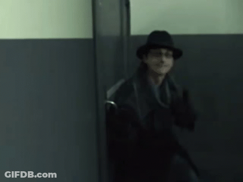 A Man In A Hat And Coat Is Standing In A Doorway GIF