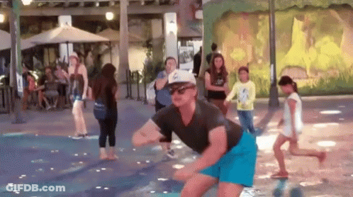A Man In A Hat And Sunglasses Is Dancing In A Water Fountain . GIF