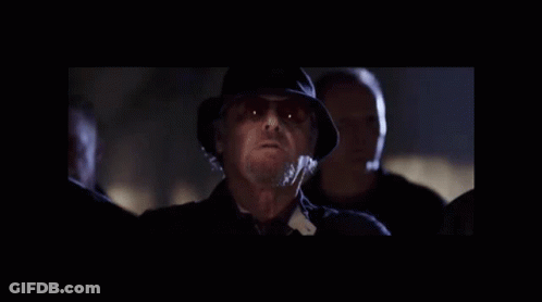 A Man In A Hat And Sunglasses Is Standing In A Dark Room . GIF