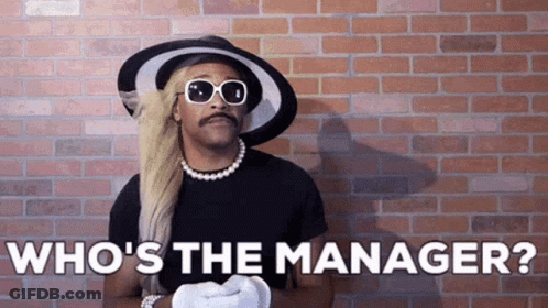 A Man In A Hat And Sunglasses Is Standing In Front Of A Brick Wall . GIF