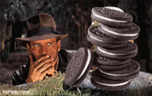 A Man In A Hat Is Covering His Mouth Behind A Stack Of Oreos GIF