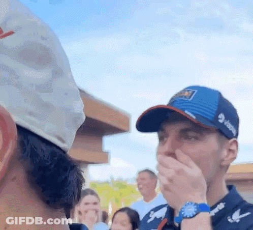 A Man In A Hat Is Covering His Mouth With His Hand While Another Man Looks On . GIF