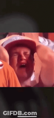 A Man In A Hat Is Crying While Sitting In A Crowd Of People . GIF