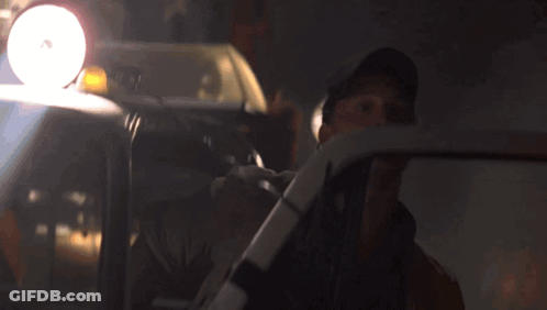 A Man In A Hat Is Driving A Car With A Light On The Top Of It GIF