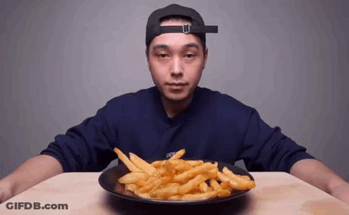 A Man In A Hat Is Eating French Fries From A Plate . GIF