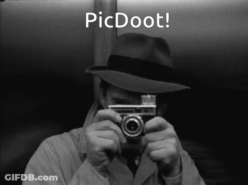 A Man In A Hat Is Holding A Camera In Front Of His Face With The Words Picdoot Below Him GIF