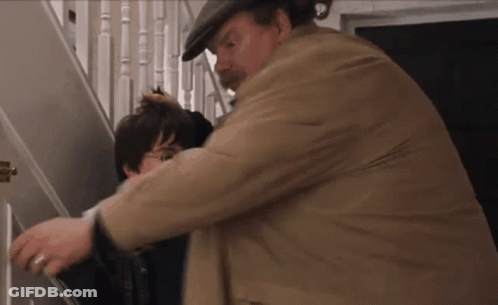 A Man In A Hat Is Holding A Child 'S Head While Standing On A Set Of Stairs . GIF