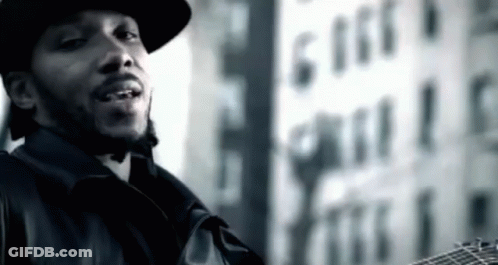A Man In A Hat Is Holding A Guitar In Front Of A Building That Says 616 GIF