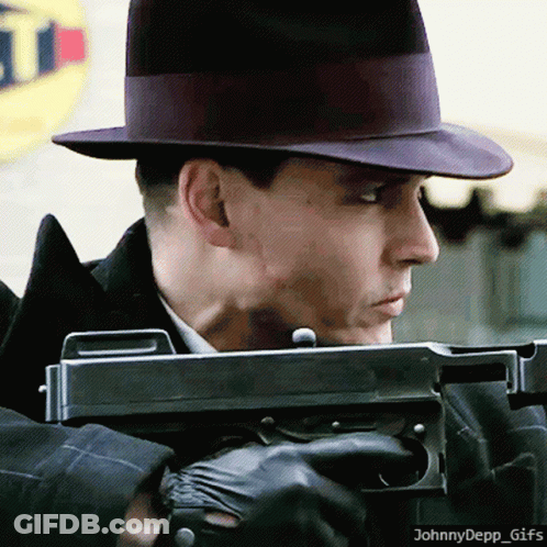 A Man In A Hat Is Holding A Gun In Front Of A Sign That Says ' T ' On It GIF