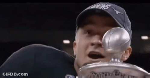 A Man In A Hat Is Holding A Trophy With A Football In His Hand . GIF