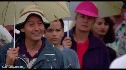 A Man In A Hat Is Holding An Umbrella In A Crowd GIF