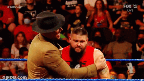 A Man In A Hat Is Hugging Another Man In A Red Shirt In A Wrestling Ring GIF