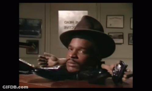 A Man In A Hat Is Laying On A Desk In Front Of A Sign That Says " Cash " GIF