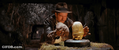 A Man In A Hat Is Looking At A Gold Object In His Hands GIF