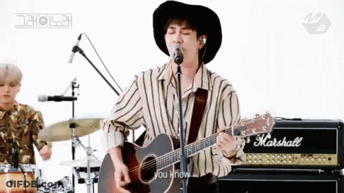 A Man In A Hat Is Playing An Acoustic Guitar In Front Of A Microphone . GIF