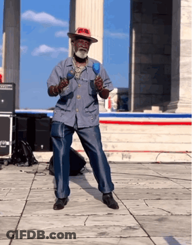 A Man In A Hat Is Playing Maracas On A Stage GIF