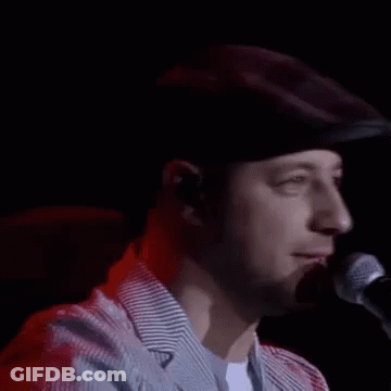 A Man In A Hat Is Singing Into A Microphone . GIF