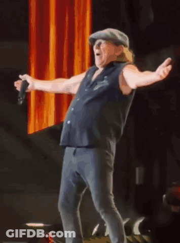 A Man In A Hat Is Singing Into A Microphone With His Arms Outstretched GIF