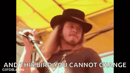 A Man In A Hat Is Singing Into A Microphone With The Words `` And This Bird You Cannot Change '' Behind Him . GIF