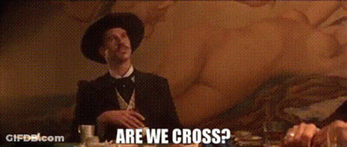 A Man In A Hat Is Sitting At A Table With The Words Are We Cross Written On The Screen Behind Him . GIF
