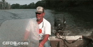 A Man In A Hat Is Sitting In A Boat On A Lake GIF