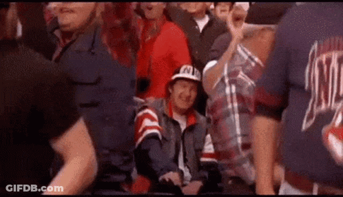 A Man In A Hat Is Sitting In The Stands Watching A Game . GIF