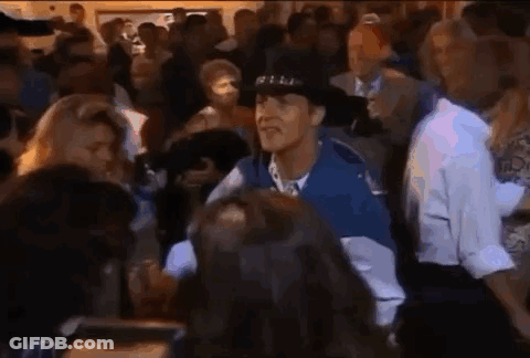 A Man In A Hat Is Standing In A Crowd Of People . GIF