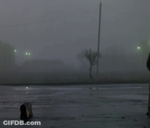 A Man In A Hat Is Standing In A Parking Lot GIF