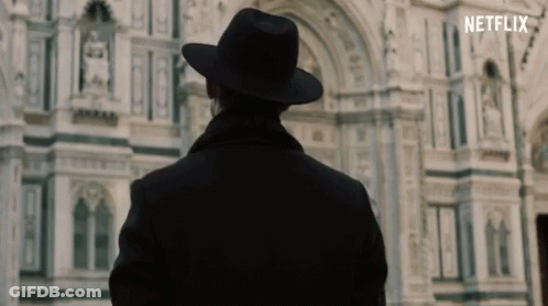 A Man In A Hat Is Standing In Front Of A Building That Says Netflix On The Bottom GIF