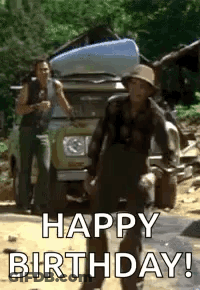 A Man In A Hat Is Standing In Front Of A Car And Says `` Happy Birthday '' . GIF