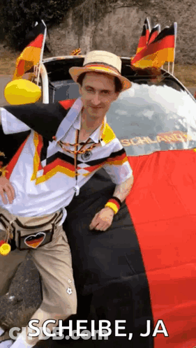 A Man In A Hat Is Standing In Front Of A Car With A German Flag On The Back . GIF
