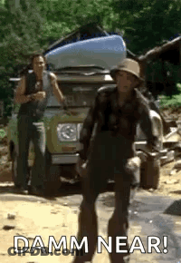 A Man In A Hat Is Standing In Front Of A Car With A Kayak On Top Of It . GIF