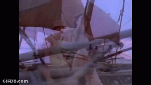 A Man In A Hat Is Standing On A Boat With A Purple Sky In The Background . GIF