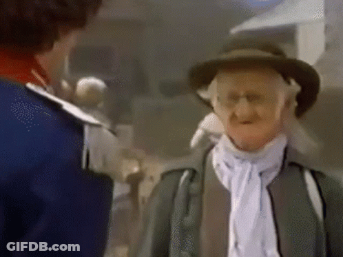 A Man In A Hat Is Talking To Another Man In A Blue Jacket . GIF
