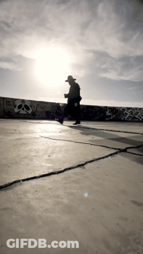Man In Hat Walking Past Skull Wall GIF