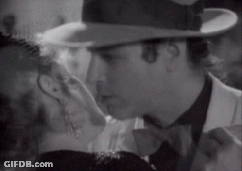 A Man In A Hat Kisses A Woman In A Black And White Photo GIF