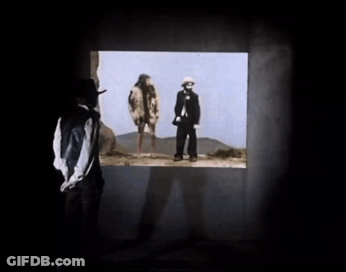 A Man In A Hat Looks Out A Window At Two People GIF