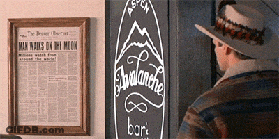 A Man In A Hat Stands In Front Of A Newspaper That Says Man Walks On The Moon GIF