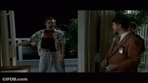 A Man In A Hawaiian Shirt Is Holding A Knife While Standing Next To A Man In A Suit And Tie . GIF