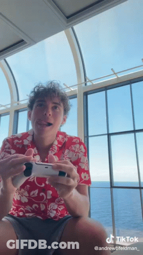 A Man In A Hawaiian Shirt Is Holding A Video Game Controller . GIF