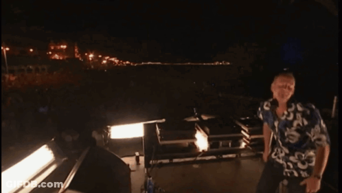 A Man In A Hawaiian Shirt Is Standing In Front Of A Stage At Night GIF